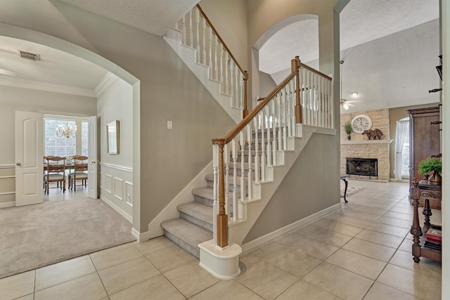 staircase with visible vents, ornamental molding, tile patterned floors, carpet, and a stone fireplace