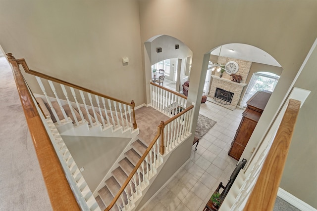 stairs with baseboards, a towering ceiling, ceiling fan, tile patterned floors, and a stone fireplace