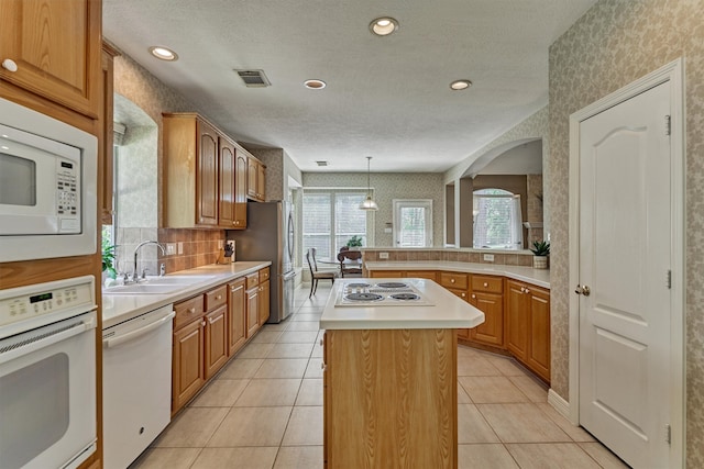 kitchen featuring a center island, decorative light fixtures, light countertops, a sink, and white appliances