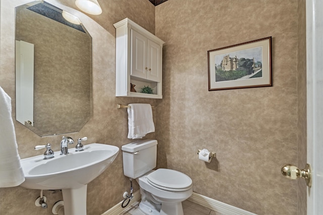 half bath featuring tile patterned flooring, baseboards, a sink, and toilet