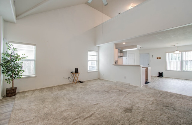 unfurnished living room featuring high vaulted ceiling, ceiling fan, and light carpet