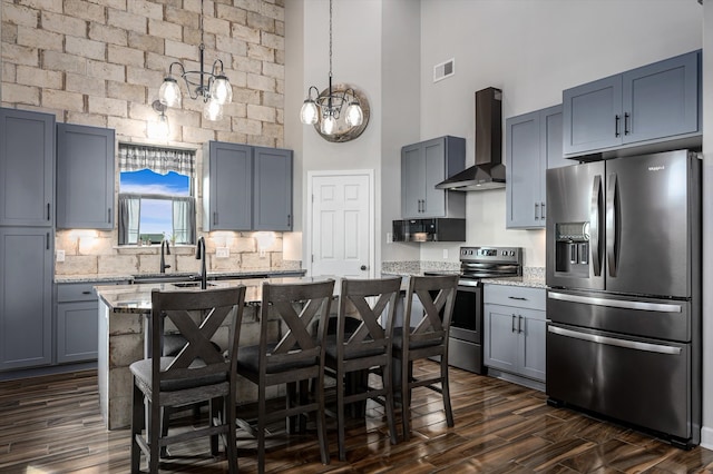 kitchen with a breakfast bar, light stone counters, wall chimney range hood, appliances with stainless steel finishes, and a high ceiling