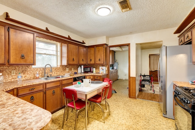 kitchen with a textured ceiling, black appliances, backsplash, light hardwood / wood-style floors, and sink