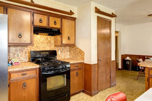 kitchen featuring black gas stove, wood walls, stainless steel fridge, and a textured ceiling