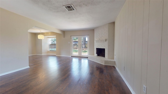 unfurnished living room with a textured ceiling, dark wood-type flooring, and a brick fireplace