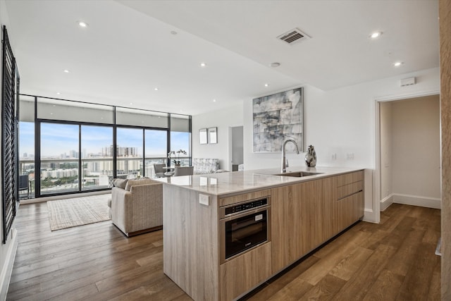 kitchen featuring light stone counters, sink, dark hardwood / wood-style floors, a wall of windows, and stainless steel oven