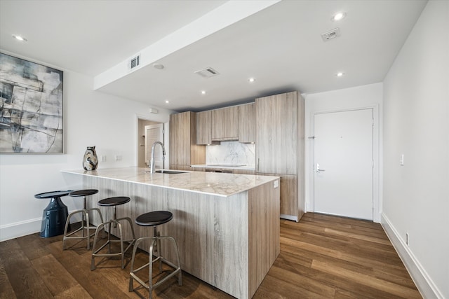 kitchen with dark hardwood / wood-style flooring, light stone counters, kitchen peninsula, sink, and a kitchen breakfast bar