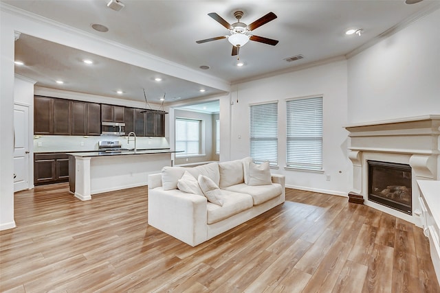 living room featuring ceiling fan, ornamental molding, light hardwood / wood-style floors, and sink