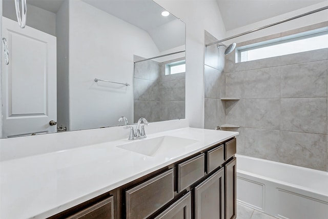 bathroom with tiled shower / bath combo, vanity, lofted ceiling, and a wealth of natural light