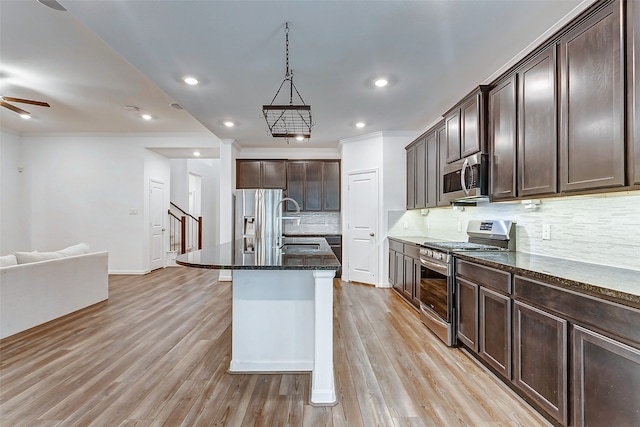 kitchen with light wood-type flooring, an island with sink, stainless steel appliances, and ceiling fan