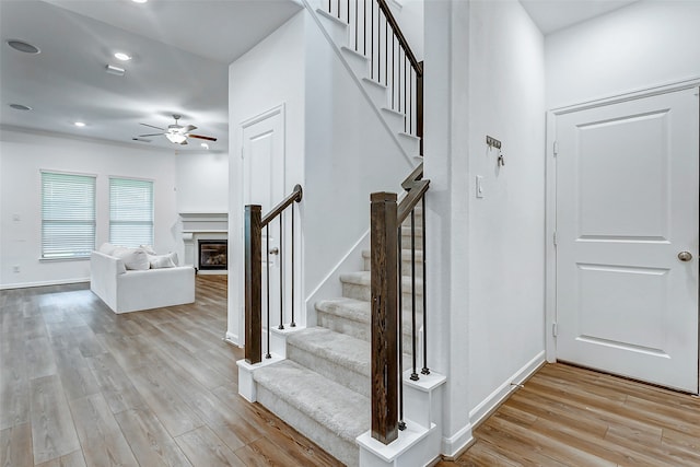 stairway with hardwood / wood-style floors and ceiling fan