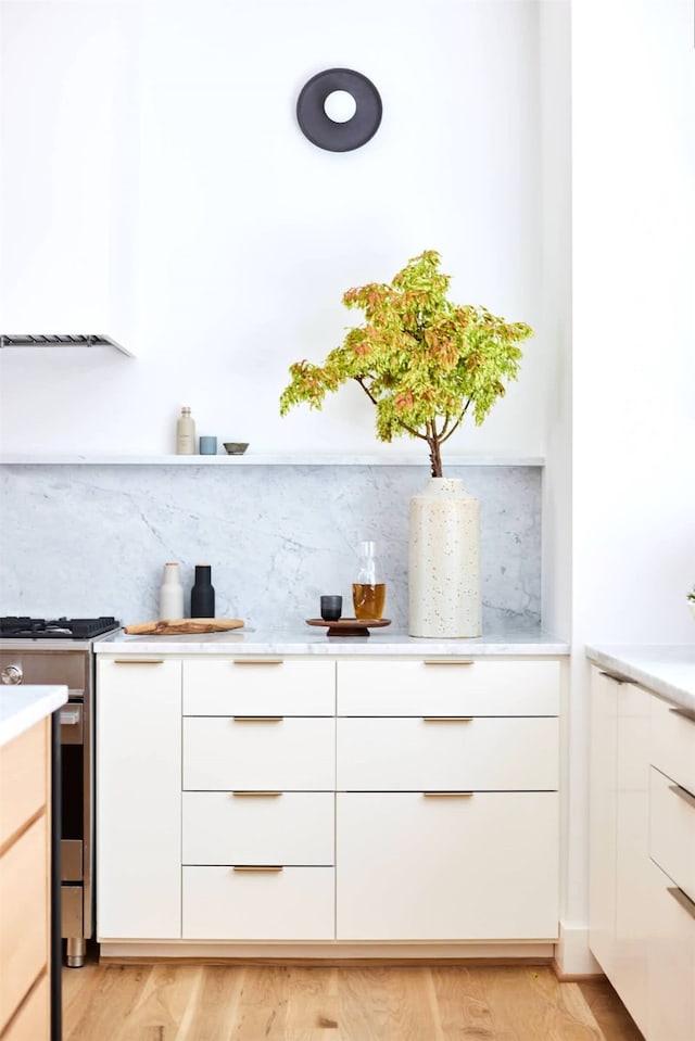 bar featuring tasteful backsplash, light wood-type flooring, gas stove, and white cabinets