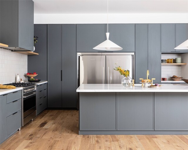 kitchen featuring gray cabinetry, light hardwood / wood-style floors, hanging light fixtures, stainless steel appliances, and decorative backsplash