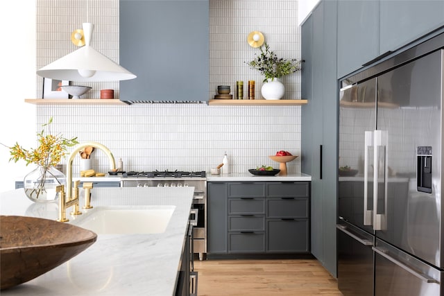 kitchen featuring light stone counters, sink, stainless steel built in refrigerator, gray cabinetry, and light hardwood / wood-style floors