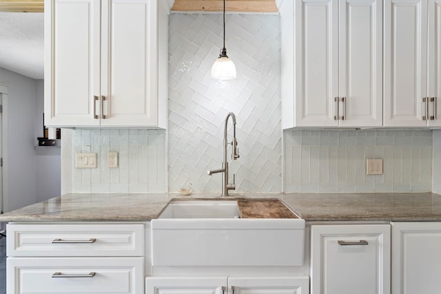 kitchen featuring light stone countertops, white cabinetry, sink, pendant lighting, and tasteful backsplash