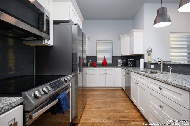 kitchen featuring decorative light fixtures, light hardwood / wood-style flooring, stainless steel appliances, light stone counters, and white cabinets