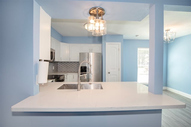 kitchen with kitchen peninsula, white cabinetry, appliances with stainless steel finishes, a notable chandelier, and decorative backsplash