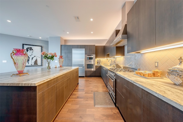 kitchen with light hardwood / wood-style flooring, high end appliances, sink, wall chimney exhaust hood, and decorative backsplash