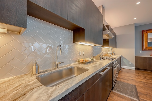 kitchen with dark brown cabinets, light hardwood / wood-style flooring, backsplash, sink, and light stone counters