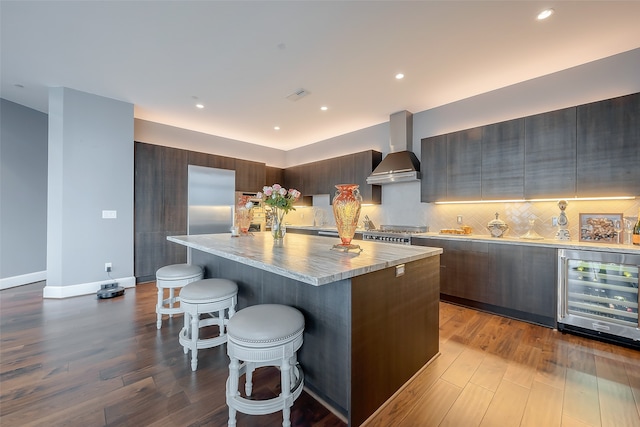 kitchen with a kitchen island, a kitchen breakfast bar, beverage cooler, light hardwood / wood-style floors, and wall chimney range hood