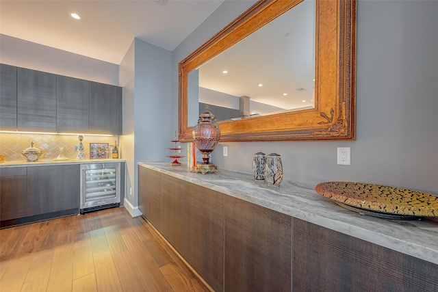 kitchen featuring beverage cooler, light stone countertops, light wood-type flooring, and tasteful backsplash