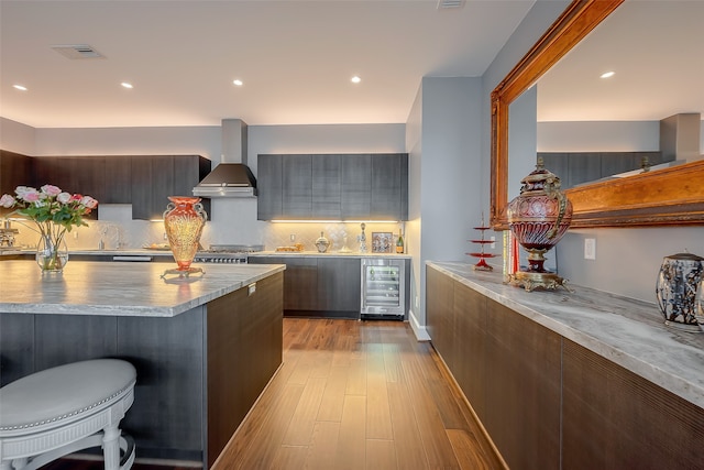 kitchen featuring beverage cooler, wall chimney exhaust hood, dark brown cabinets, and light hardwood / wood-style floors