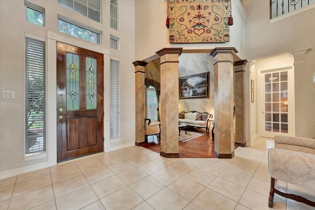 foyer entrance with a towering ceiling, light tile patterned flooring, and decorative columns