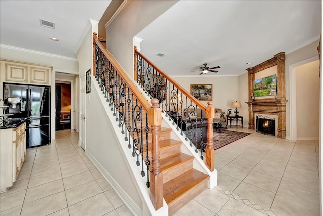 stairs with crown molding, ceiling fan, tile patterned floors, and a fireplace