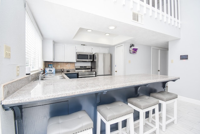 kitchen with kitchen peninsula, appliances with stainless steel finishes, a breakfast bar, white cabinetry, and sink