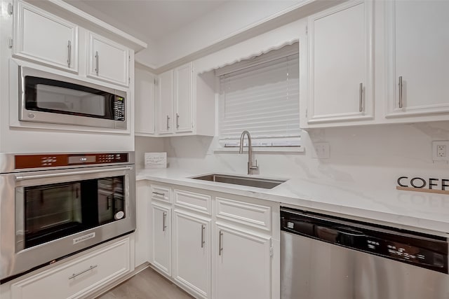 kitchen with light stone countertops, appliances with stainless steel finishes, sink, and white cabinetry