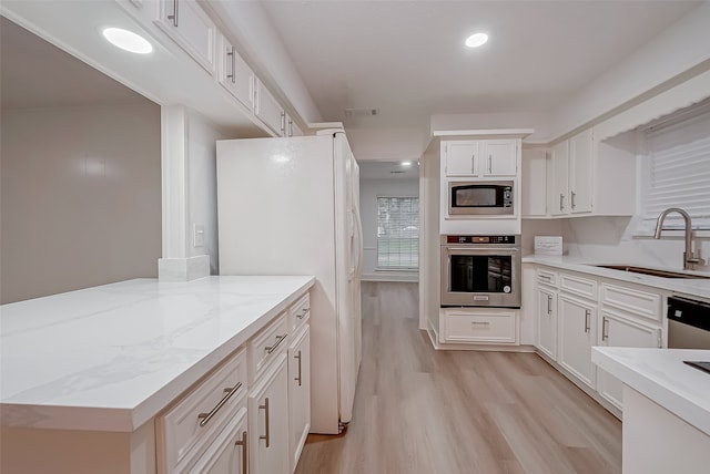 kitchen with light wood-type flooring, light stone counters, sink, white cabinetry, and stainless steel appliances