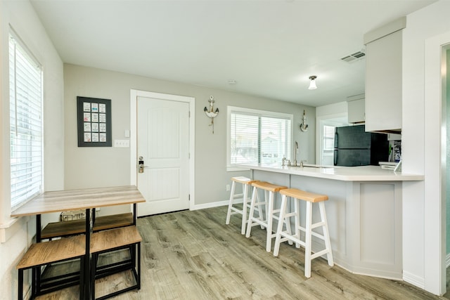 kitchen featuring light hardwood / wood-style flooring, kitchen peninsula, white cabinets, and black fridge