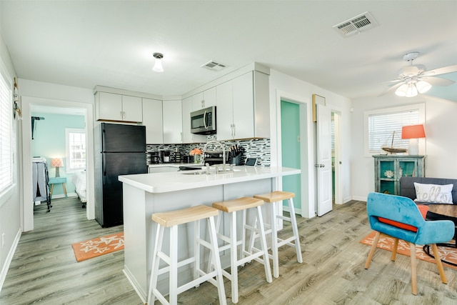 kitchen featuring white cabinetry, tasteful backsplash, a kitchen bar, light hardwood / wood-style flooring, and black refrigerator