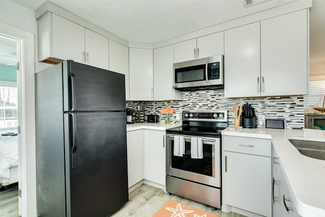 kitchen with white cabinets, appliances with stainless steel finishes, backsplash, and light hardwood / wood-style flooring