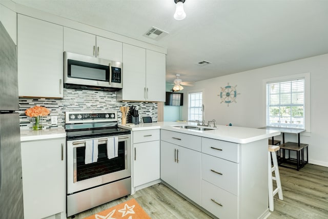 kitchen with kitchen peninsula, stainless steel appliances, ceiling fan, and light hardwood / wood-style floors