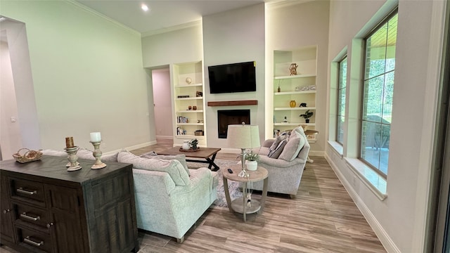 living room with built in features, wood-type flooring, crown molding, and a healthy amount of sunlight