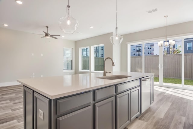 kitchen with stainless steel dishwasher, sink, decorative light fixtures, light hardwood / wood-style flooring, and an island with sink