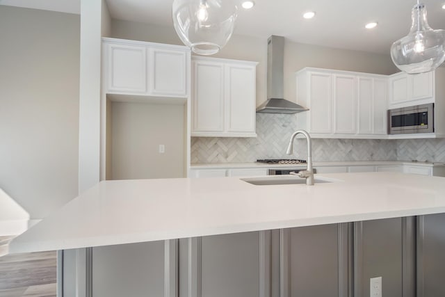 kitchen with white cabinets, stainless steel microwave, wall chimney exhaust hood, and an island with sink