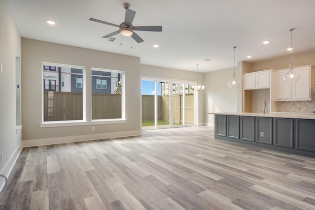 unfurnished living room featuring ceiling fan with notable chandelier, light hardwood / wood-style floors, and sink