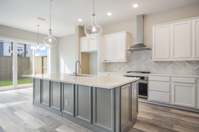 kitchen with light hardwood / wood-style floors, white cabinetry, a kitchen island with sink, and wall chimney exhaust hood