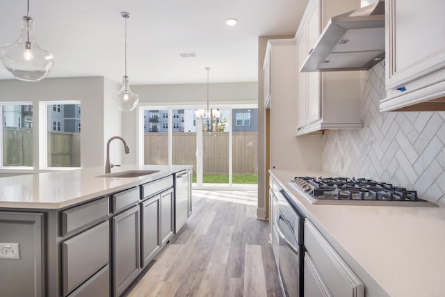 kitchen with decorative backsplash, light wood-type flooring, wall chimney exhaust hood, stainless steel appliances, and sink