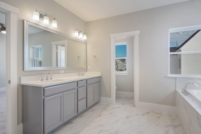 bathroom with tiled tub, vanity, and toilet