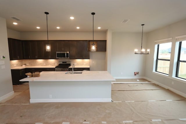 kitchen featuring decorative backsplash, stainless steel appliances, sink, hanging light fixtures, and an island with sink