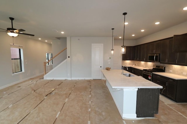 kitchen featuring ceiling fan, tasteful backsplash, an island with sink, decorative light fixtures, and appliances with stainless steel finishes