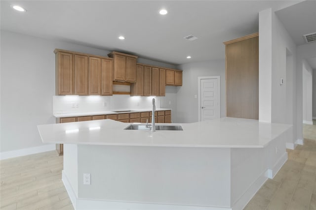 kitchen featuring a large island with sink, sink, and light hardwood / wood-style flooring