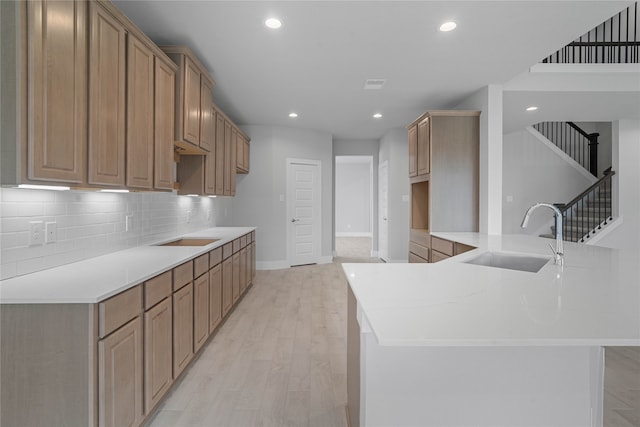 kitchen featuring backsplash, a center island with sink, sink, and light hardwood / wood-style flooring