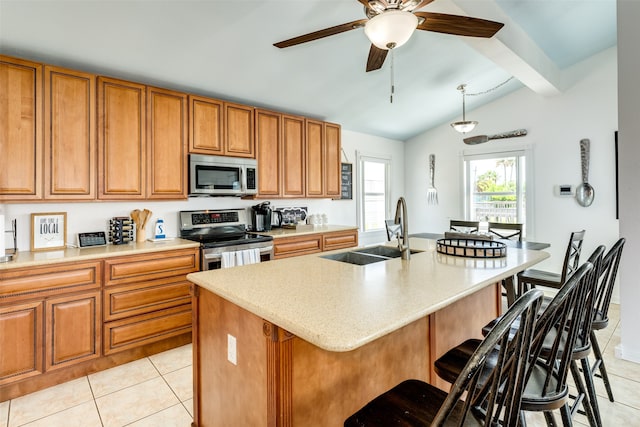 kitchen with a breakfast bar area, appliances with stainless steel finishes, an island with sink, sink, and ceiling fan