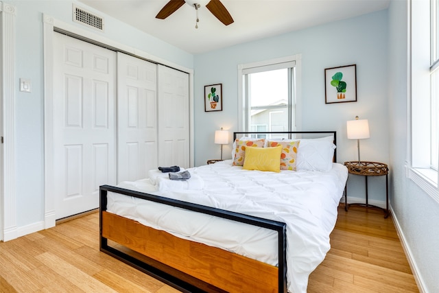 bedroom with multiple windows, light hardwood / wood-style flooring, ceiling fan, and a closet