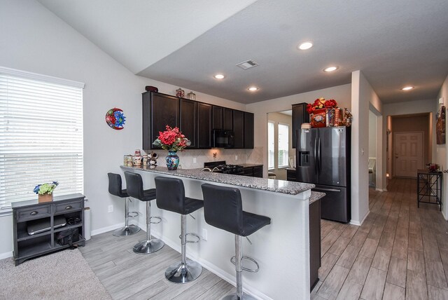 kitchen featuring a kitchen breakfast bar, vaulted ceiling, kitchen peninsula, light hardwood / wood-style flooring, and stainless steel fridge with ice dispenser