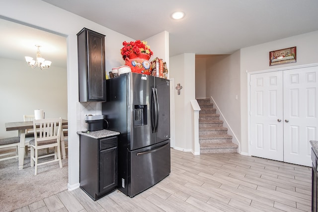 kitchen featuring light stone counters, stainless steel fridge, dark brown cabinets, an inviting chandelier, and light wood-type flooring